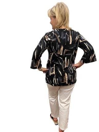 Woman wearing a black and gold patterned top and white pants in a fitting room.