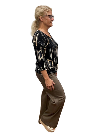 Woman standing in a fitting room wearing a patterned top and brown pants.