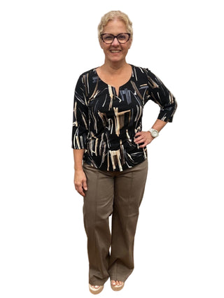Woman standing in a fitting room wearing a black patterned top and brown pants.