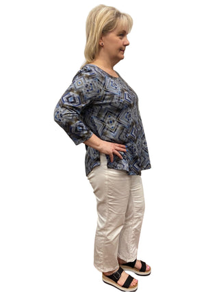 Woman wearing a blue patterned top and white pants standing in a fitting room.