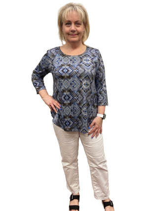 Woman wearing a blue patterned top and white pants in a fitting room.