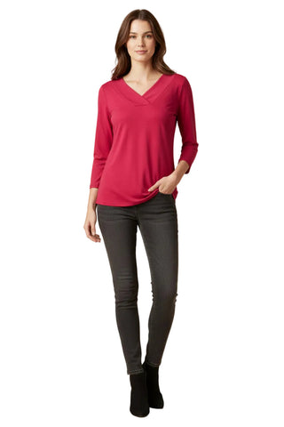 A woman modeling a bright pinkish-red long-sleeve V-neck top with dark gray skinny jeans and black ankle boots, standing against a plain white background.