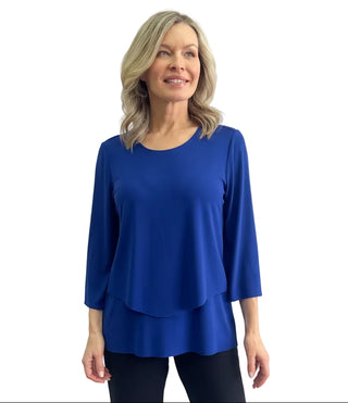 A woman modeling a bright magenta three-quarter sleeve top with a layered, asymmetrical hem against a light gray studio background.