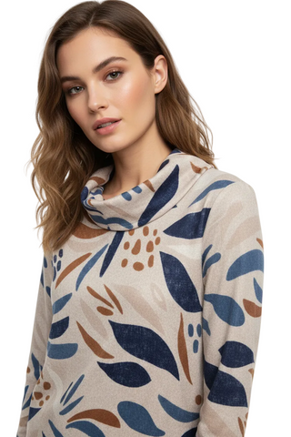 A woman wearing a beige cowl-neck sweater with a blue and brown abstract botanical pattern, photographed against a clean white studio background.