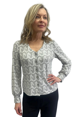 A woman modeling a long-sleeve knit cardigan with a gray and white geometric pattern, featuring a V-neck and button closure, paired with black pants against a plain light gray background.