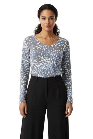A woman modeling a long-sleeve crewneck top with a blue and white leaf pattern, paired with black wide-leg trousers, against a plain light gray studio background.
