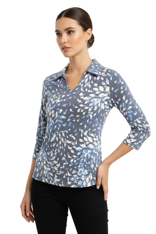 A woman modeling a three-quarter sleeve button-up blouse with a blue, gray, and white leaf pattern, paired with black pants, against a plain light gray studio background.