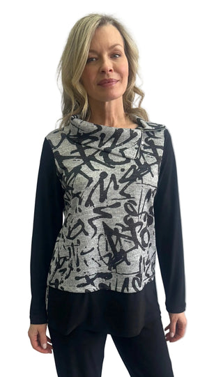 A woman modeling a long-sleeve top with a black and white abstract graffiti-style pattern on the front and solid black sleeves, paired with black pants, against a light gray studio background.