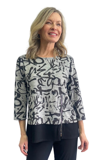 A woman modeling a three-quarter sleeve top with a black abstract graffiti-style print on a heather gray background, paired with black pants, against a light gray studio backdrop.
