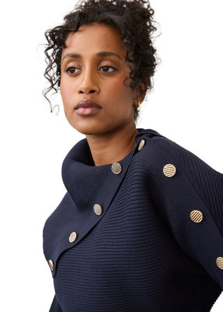 A close-up portrait of a model wearing a navy blue ribbed knit cowl-neck top with decorative gold buttons.