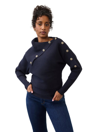 A woman modeling a dark navy ribbed knit sweater with asymmetrical button details on the shoulder and sleeve, paired with dark blue jeans against a plain light gray background.