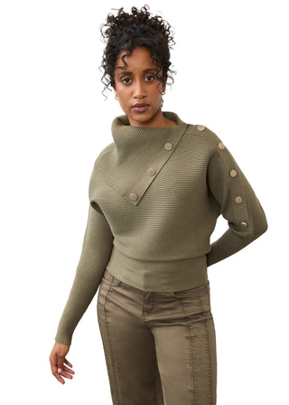 A woman modeling a ribbed knit asymmetrical sweater in olive green with large decorative buttons, paired with matching olive pants, against a plain light gray studio background.