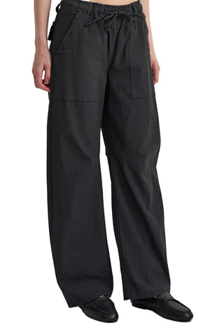A person wearing loose black wide-leg pants with an elastic drawstring waist and large front patch pockets, paired with black shoes, against a plain light background.