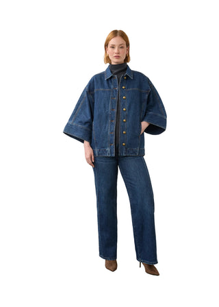 A model stands in a studio wearing a dark blue denim jacket with wide sleeves, matching wide-leg denim jeans, a black turtleneck, and brown pointed-toe heels.