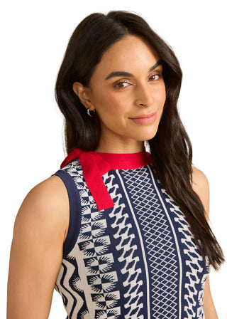 Woman wearing a sleeveless dress with a red bow and patterned design on a beige background
