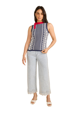 Woman wearing a sleeveless patterned top and light gray pants on a beige background