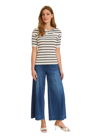 Woman wearing a striped shirt and blue jeans against a beige background