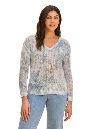Woman wearing a patterned long-sleeve top and jeans on a beige background