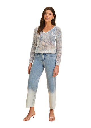 Woman wearing a light blue patterned top and jeans on a beige background