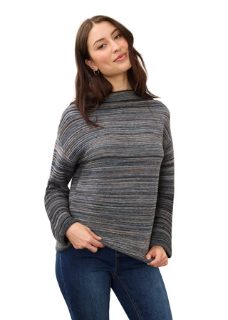 A woman modeling a long-sleeve knit sweater with horizontal gray, blue, and beige stripes, paired with dark blue jeans, against a plain light gray background.