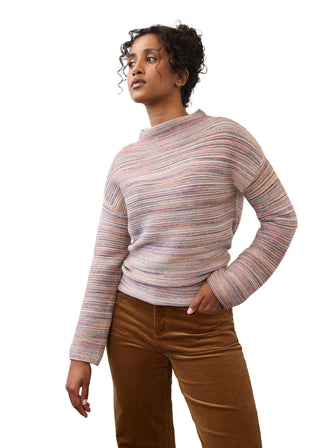 A woman wearing a long-sleeve knit sweater with horizontal multicolor stripes in pink, blue, yellow, and green, paired with brown corduroy pants, standing against a plain light gray studio background.