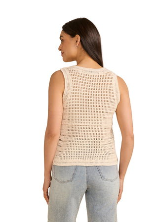 Woman wearing a sleeveless crochet top and jeans on a beige background