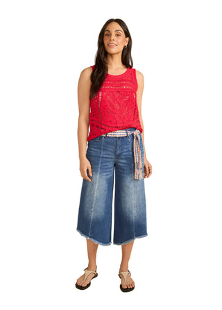 Woman wearing a red sleeveless top and blue denim culottes on a beige background