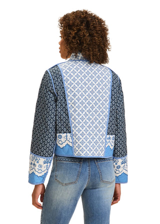 Person wearing a blue patterned jacket and jeans on a beige background