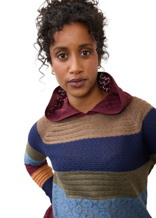 A woman wearing a multi-colored striped knit sweater with a burgundy lace-trimmed collar, photographed against a plain white studio background.