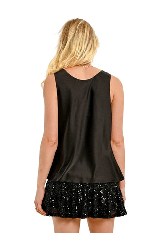 Woman wearing a black sleeveless top and black sequin skirt on a beige background
