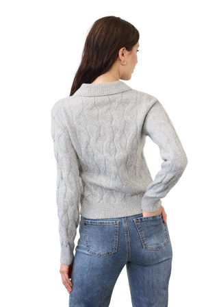 A woman shown from the back wearing a light gray cable-knit sweater and blue jeans against a plain light gray studio background.