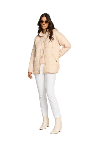 Woman wearing a beige quilted jacket, white pants, and beige boots on a light gray background
