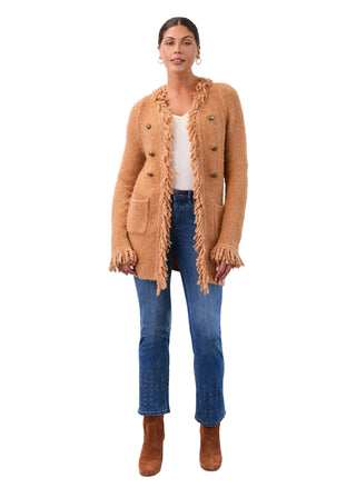 Woman wearing a brown cardigan with fringe, white shirt, blue jeans, and brown boots against a white background.