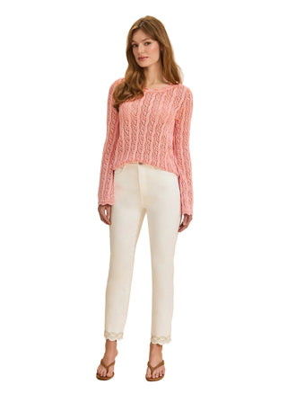Woman wearing a pink cable knit sweater and white pants on a beige background
