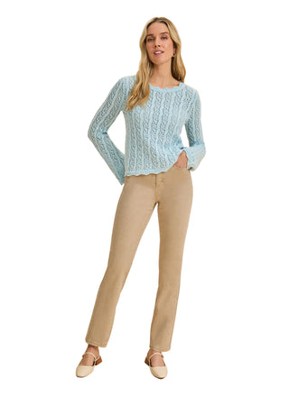 Woman wearing a light blue sweater and beige pants on a beige background