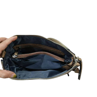 An open tan leather clutch or wristlet bag showing its navy blue interior lining, gold-tone zipper, and a hand holding the left side against a light gray background.