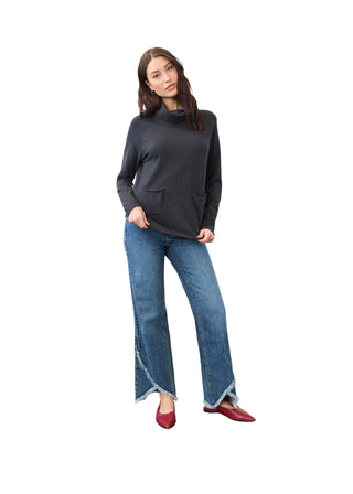 A woman modeling a dark charcoal gray mock-neck knit sweater, blue wide-leg jeans with frayed hems, and red pointed-toe flats against a plain studio background.