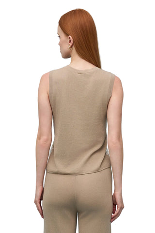 Woman wearing a beige sleeveless top and pants against a light blue background