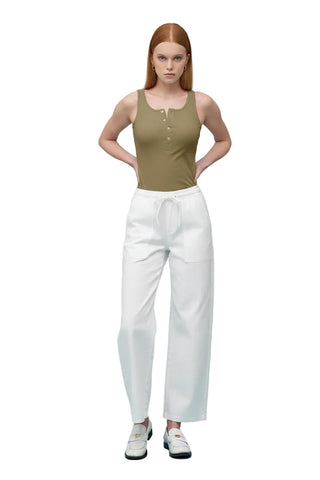 Woman wearing a white tank top and light blue pants on a light blue background