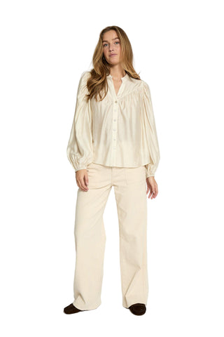 Woman wearing a cream satin pajama set on a white background