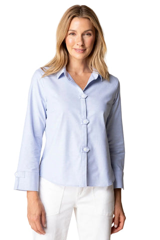 Woman wearing a light blue button-up shirt and white pants against a beige background