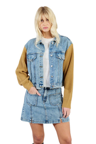 Woman wearing a denim jacket and skirt with a mustard yellow long-sleeve shirt on a gray background