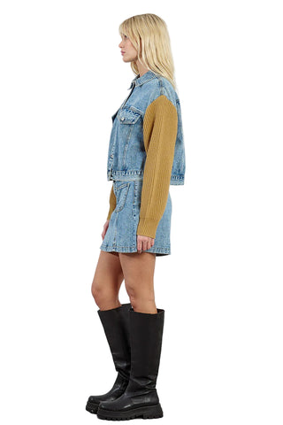 Woman wearing a denim dress with yellow sleeves and black knee-high boots on a white background