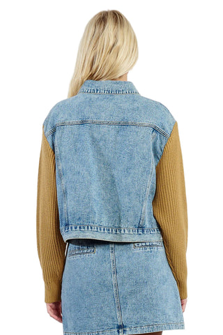 Person wearing a denim jacket over a mustard yellow sweater and skirt on a white background