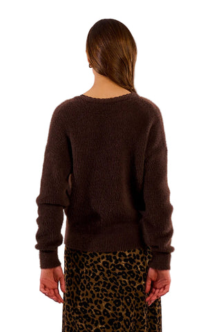 Person wearing a dark brown sweater and leopard print pants against a plain background