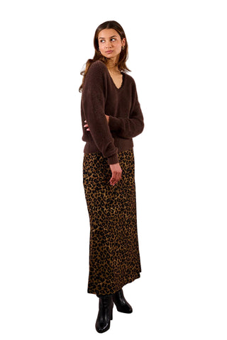 Woman wearing a brown sweater and leopard print skirt against a plain background