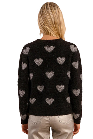 Black sweater with heart patterns worn by a person on a beige background