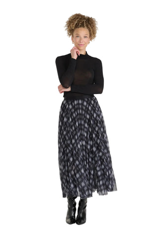 A woman modeling a black mock-neck long-sleeve top and a black and gray patterned pleated midi skirt, paired with black ankle boots, against a light gray studio background.