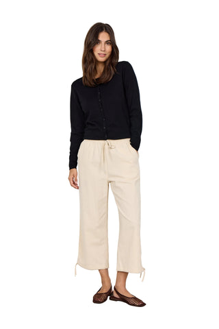 Woman wearing a black top and beige pants against a white wall