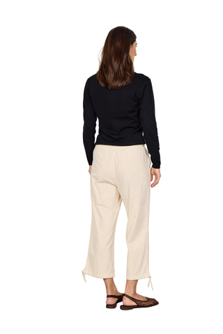 Woman wearing a black top and beige pants against a white background